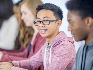 pre-teens working in a classroom - boy in glasses smiles at camera