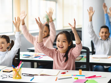 pre-teens in class with smiles and hands up!