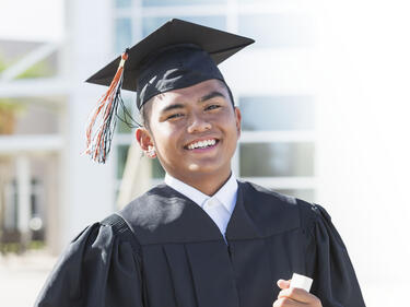Man in grad cap and gown with diploma